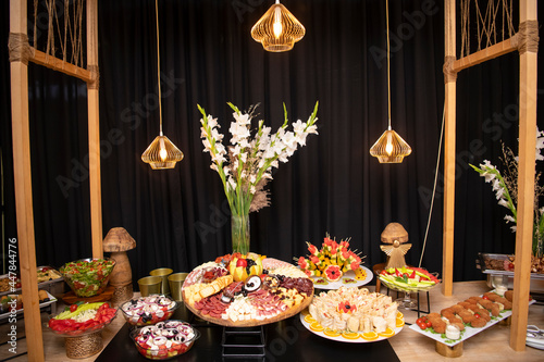 Delicious handmade appertizer catering food on a wooden table and construction with luxury decoration and lights in background. 