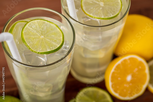 A close up picture of two refreshing glasses of cold fruit juice with straw, ice lime and lemon juice, decorating with fresh lime and lemon on wooden table. Concept for refreshing