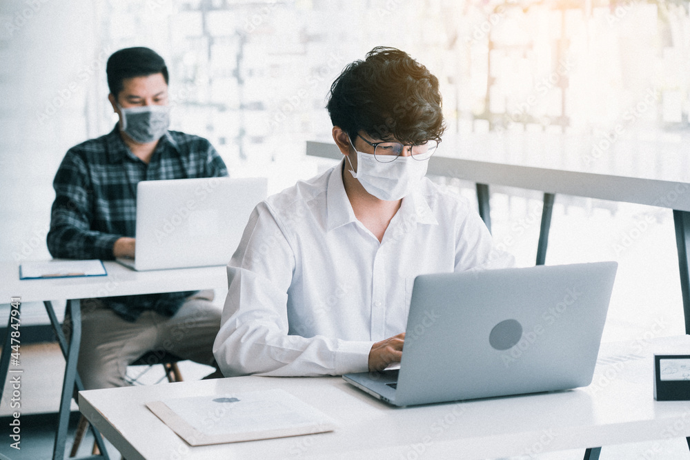 Asian colleague works while wearing a mask in the office during COVID-19. Asian colleague works while wearing a mask in the office during COVID-19.