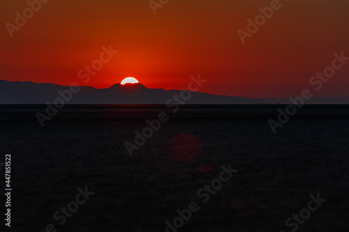 Scarlet sunrise on the large endorheic salt lake Chott el Djerid in the Sahara desert of southern Tunisia with the Atlas Mountains on the background
