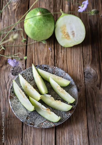 Barattieri are kind of Italian cucumber, sliced on the plate, wooden table, wild flowers