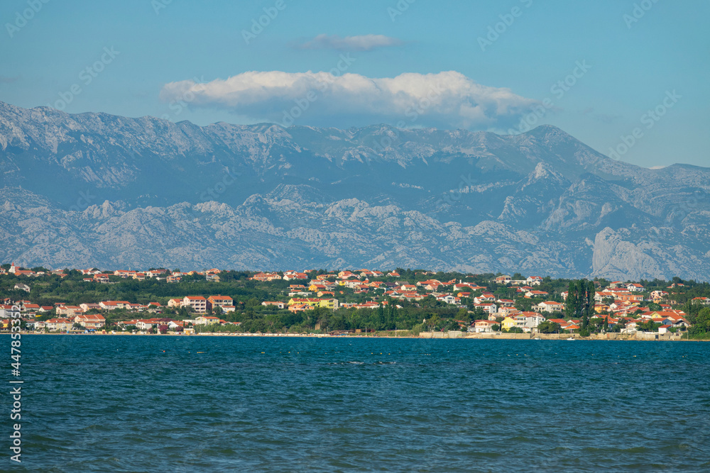 Seafront vacation houses sprawl along the coast beneath Velebit mountain range