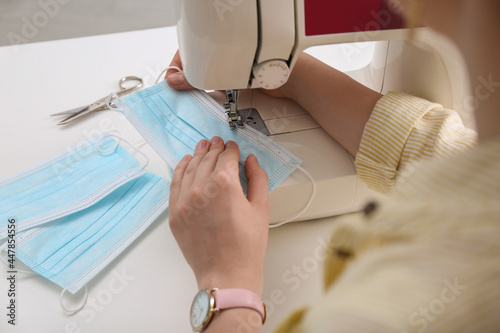 Woman making disposable mask with sewing machine at white table, closeup