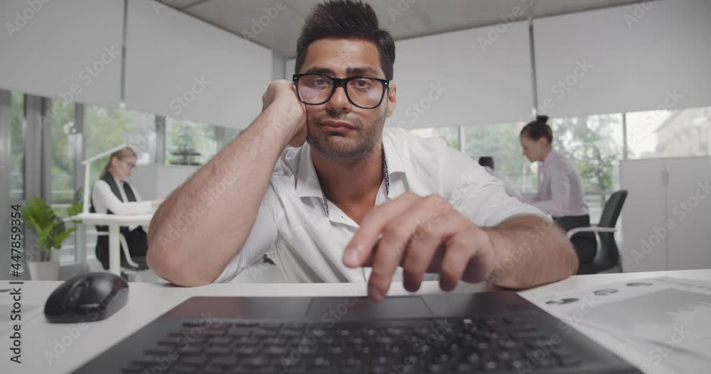 Bored or tired young bearded entrepreneur reading report or article on laptop screen