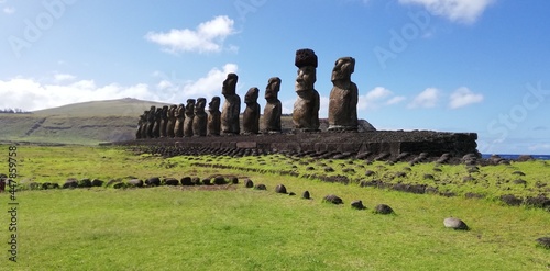 13 moai in Ahu Tongariki, Easter Island. Giant monoliths enclosed between a green lawn and the blue ocean behind them.