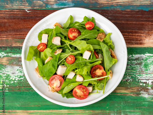 Fresh spinach salad with tomato, small pieces of herb roasted chicken in white ceramic dish on colourful wooded table. Concept for healthy. Studio picture