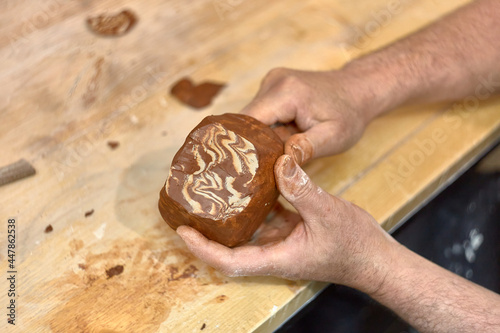Hands of a ceramist who cuts a cup made in Japanese technique Nerikomi from red and light clay to develop the pattern