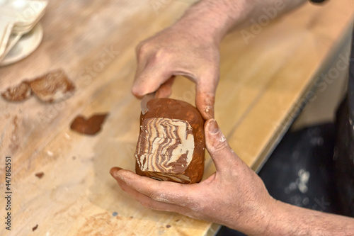 Hands of a ceramist who cuts a cup made in Japanese technique Nerikomi from red and light clay to develop the pattern