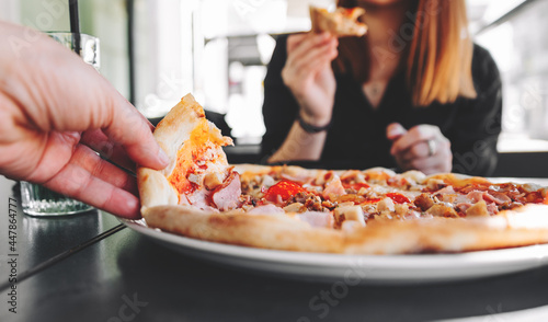 man Hand takes a slice of meat Pizza with Mozzarella cheese, salami, Tomatoes, pepper, ham, Spices and chicken in cafe
