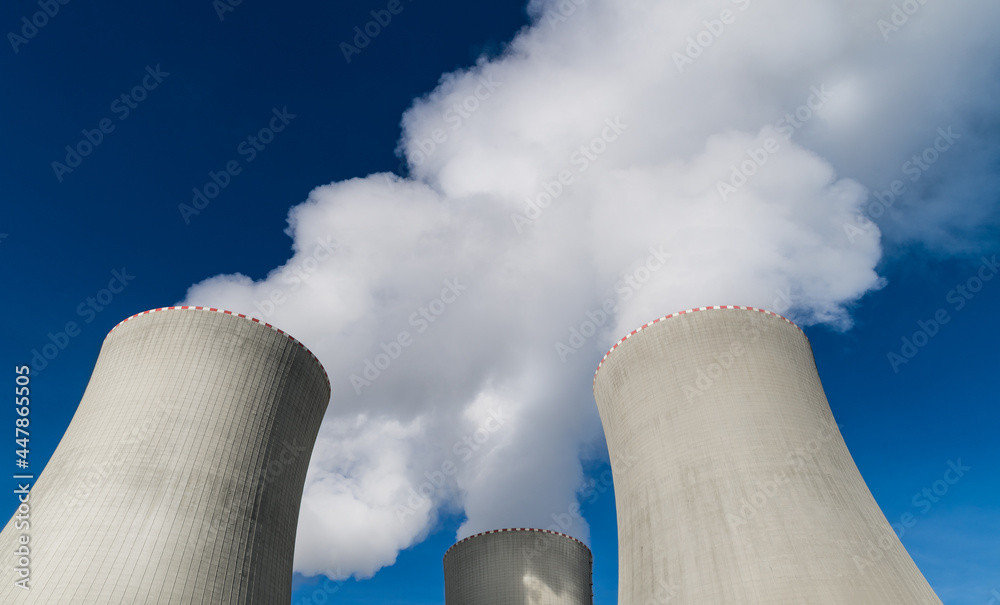 Closeup of nuclear power plant cooling towers belching out white plume of  water vapor. Top detail of large concrete structures removing heat from  modern generating station on blue sky background. Eco. Stock