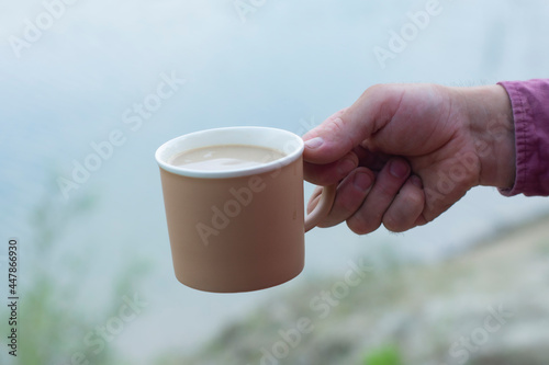 Man holds a mug with coffee in his hands on the background of nature.
