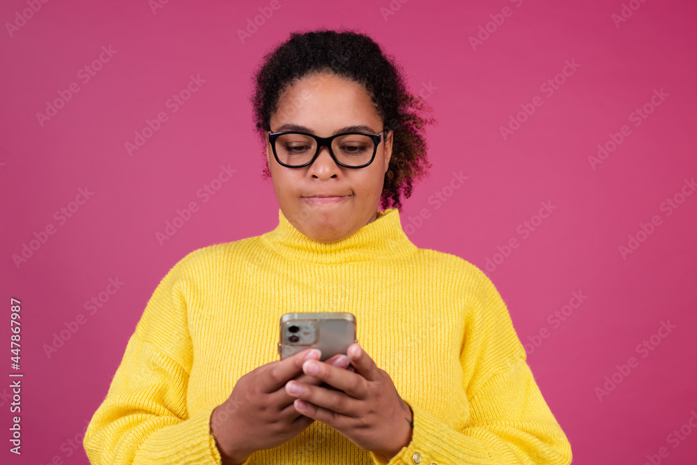 Beautiful african american woman on pink background typing message on mobile phone focused thoughtful Beautiful african american woman on pink background typing message on mobile phone focused thoughtful