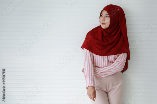 Confident young ethnic woman in Muslim headscarf smiling against white wall