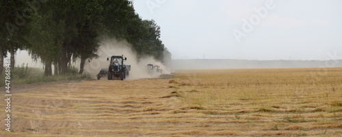 Golden linen field edge road with fast drive tractors in dust cloud on , linum harvesting in East Europe at summer day photo