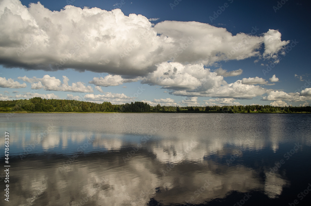 Dramatic sky with white clouds, reflection, lake and forest, Latvia. 