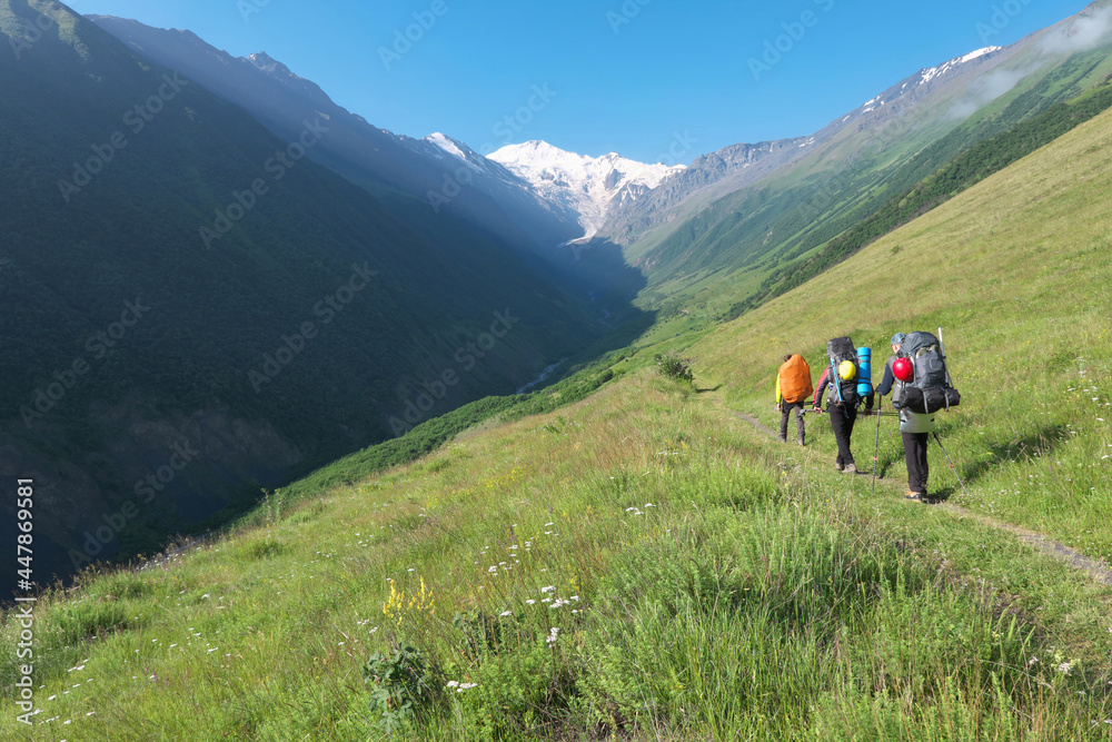 Group of tourists (climbers) walk towards Mount Kazbek through Genaldon river gorge on sunny summer day. North Ossetia–Alania, Caucasus, Russia.