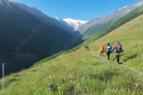 Group of tourists (climbers) walk towards Mount Kazbek through Genaldon river gorge on sunny summer day. North Ossetia–Alania, Caucasus, Russia.
