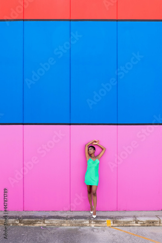 Stylish young black woman with electric green dress and white heels in front of a multicolored background
