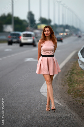 Alone beautiful woman in pink dress standing at the road