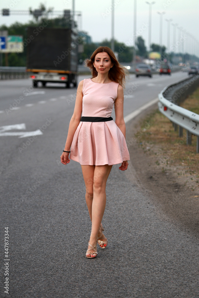 Alone beautiful woman in pink dress standing at the road