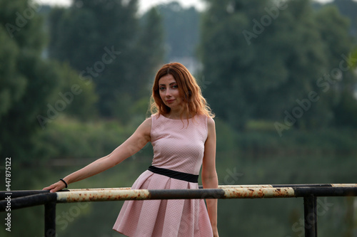 Portrait of beautiful woman in pink dress standing on a bridge at the lake