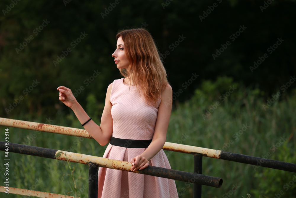 Naklejka premium Portrait of beautiful woman in pink dress standing on a bridge at the lake