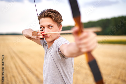 Fotografering Young male sportsman targeting with traditional bow - Teenager archer practicing