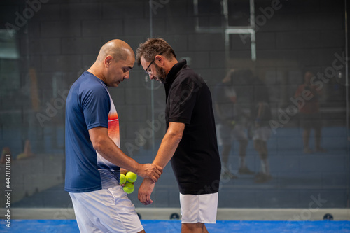 Monitor teaching padel class to man, his student - Trainer teaches boy how to play padel on indoor tennis court