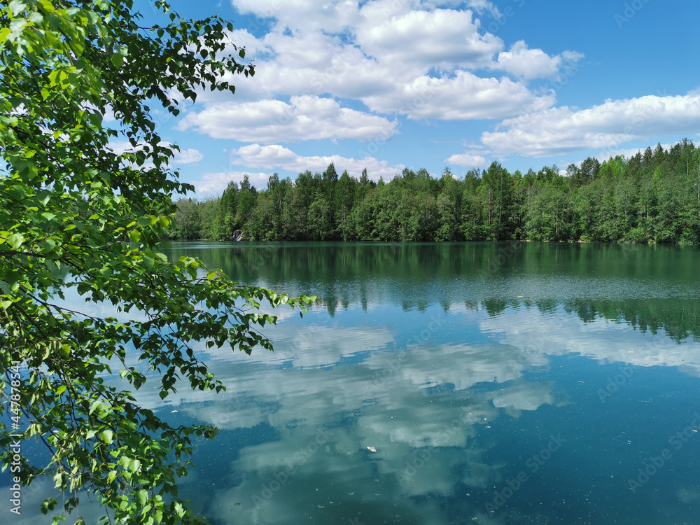 Fototapeta premium The shore of the lake Light with turquoise water, which reflects the trees and the sky with clouds, in the mountain park Ruskeala.