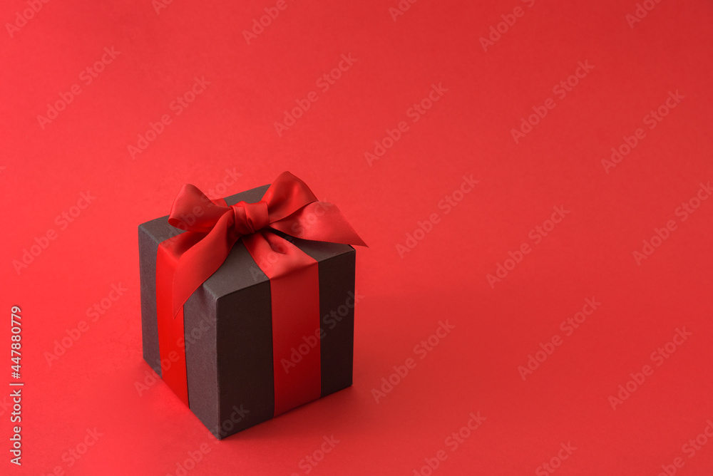 Black gift box with red bow on red background Black gift box with red bow on red background