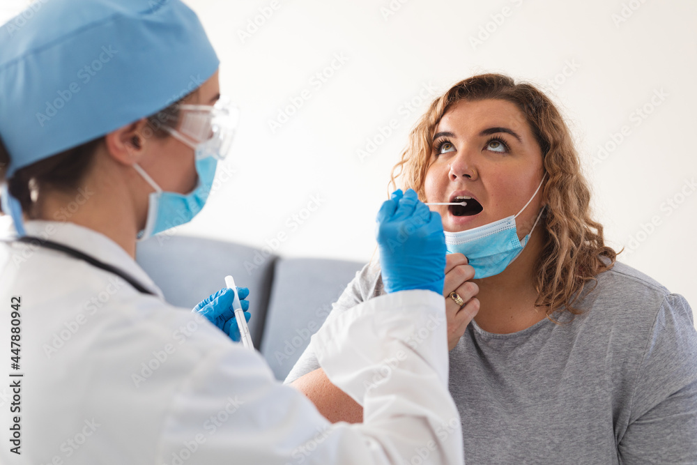 Caucasian female doctor wearing face mask taking swab test from female patient at home Caucasian female doctor wearing face mask taking swab test from female patient at home