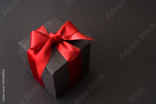 Black gift box with red bow on black background