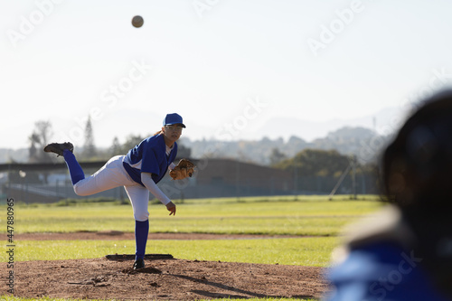Mixed race female baseball pitcher on sunny baseball field throwing ball during game photo