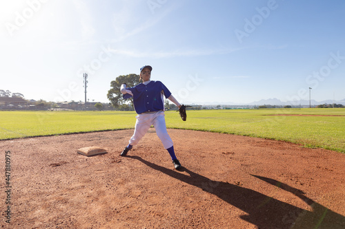 Mixed race female baseball player on sunny baseball field throwing ball during game photo