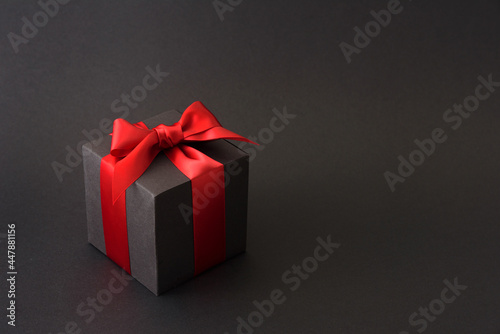 Black gift box with red bow on black background