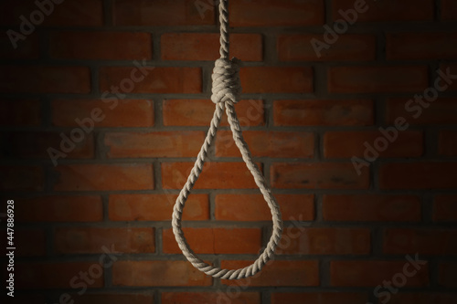 Rope noose with knot hanging near brick wall