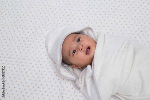 Adorable baby girl wrapped with white towel after shower. A southeast asian baby in white blanket on white background cloth. Top view. 
