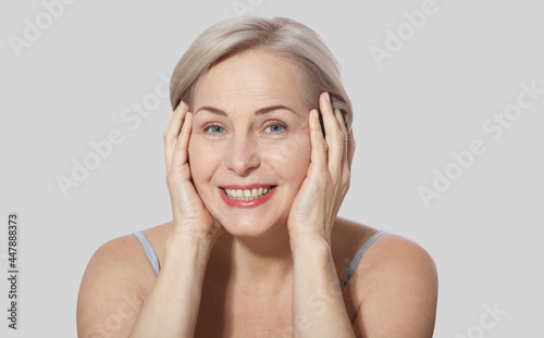 Fifty year old woman is very pleased with her well-groomed face relaxed looking at the camera. Macro face. Realistic images with their own imperfections. Isolated on grey.