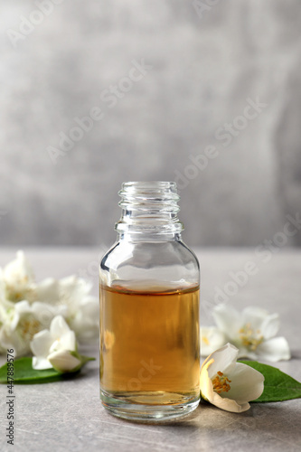 Essential oil and jasmine flowers on light grey table