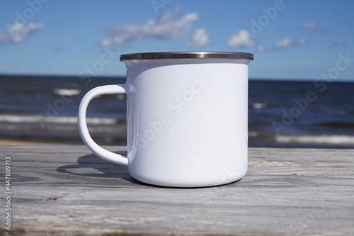 White enamel cup mockup, blank coffee mug with sea view on background, campfire cup mock up, camping, wanderlust, travel  design. photo