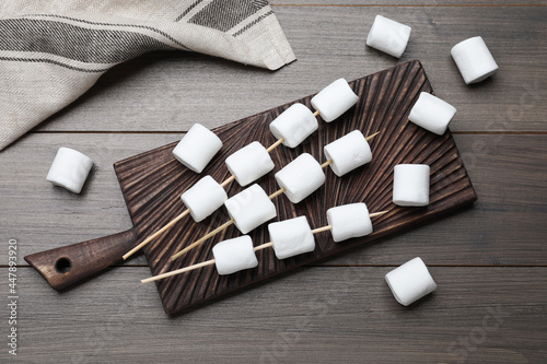 Sticks with marshmallows on wooden table, flat lay