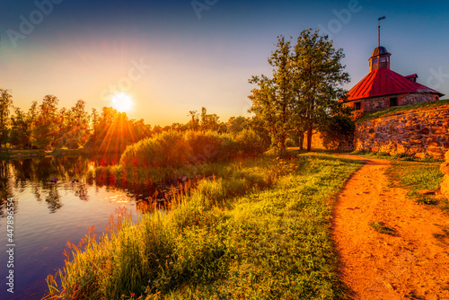Medieval fortress on the river bank. Sunset. Woodland. Blue sky. The road near the fortress wall. Beautiful nature. Korela Fortress, Priozersk, Russia. View from the side of the road.