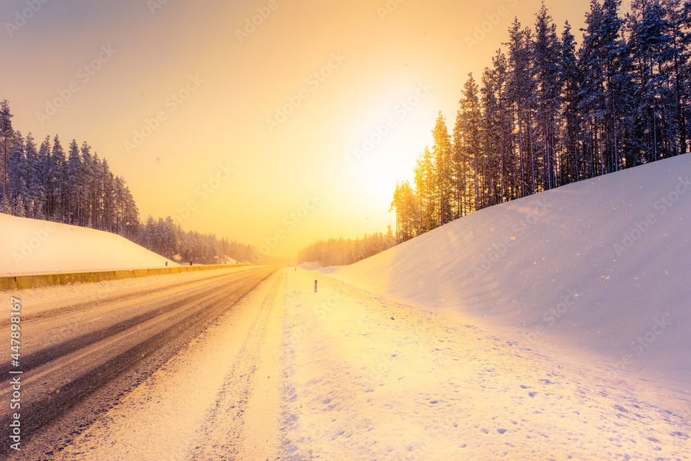 Sunrise on a clear winter morning, empty highways in snow. View from the side of the road. Coniferous forest. Russia, Europe. Beautiful nature.