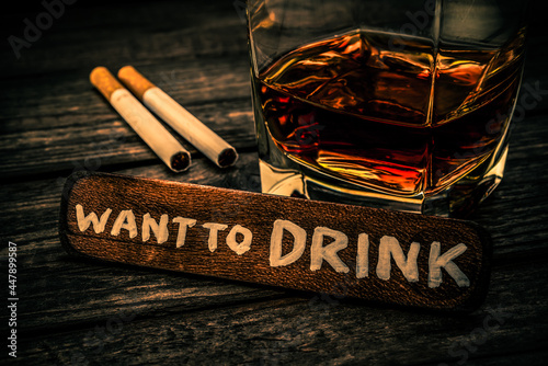 Glass of brandy with cigarettes and the wooden plank on it is an inscription "want to DRINK" on an old wooden table. Close up view, focus on the inscription