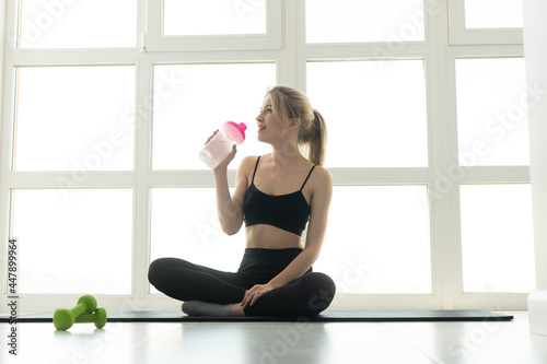 Woman drinking water from bottle on fitness mat