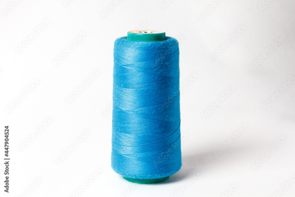 A large bobbin of blue thread on a white background A large bobbin of blue thread on a white background