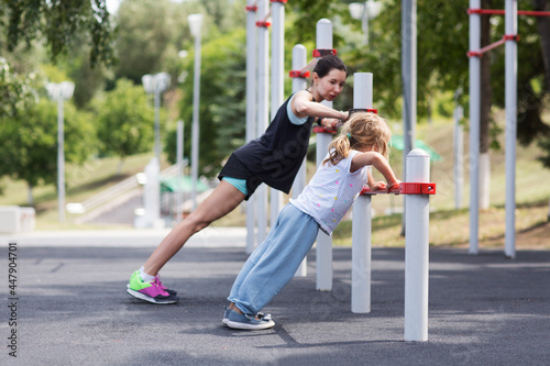 Sporty mom and daughter child girl   doing morning workout and stretching  on street sports ground. Fitness workout on the sports ground. a healthy family. © ulza