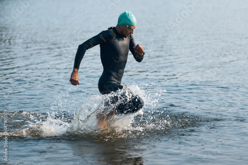 Professional triathlete swimming in river's open water. Man wearing swim equipment practicing triathlon on the beach in summer's day. photo