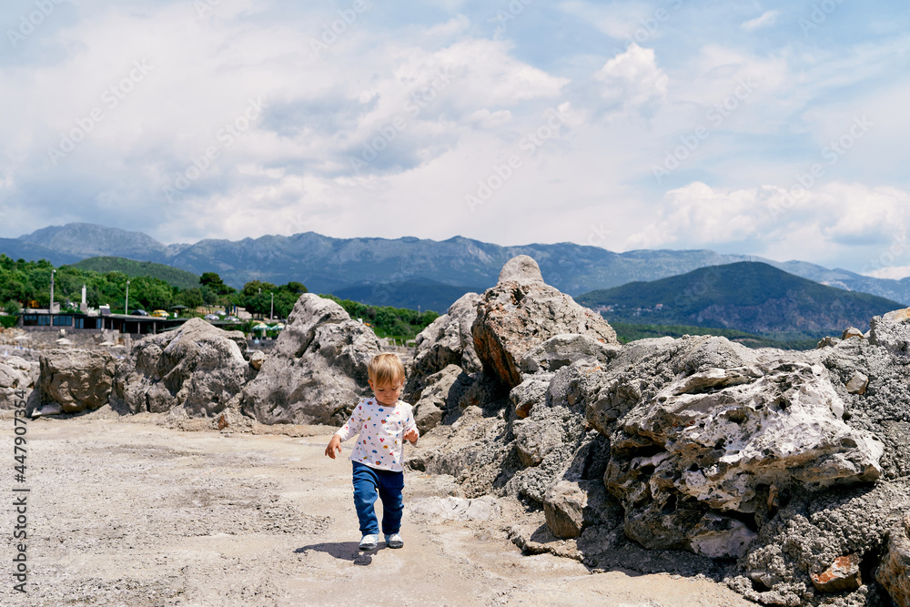 Kid walks on a stone platform with boulders against a background of mountains