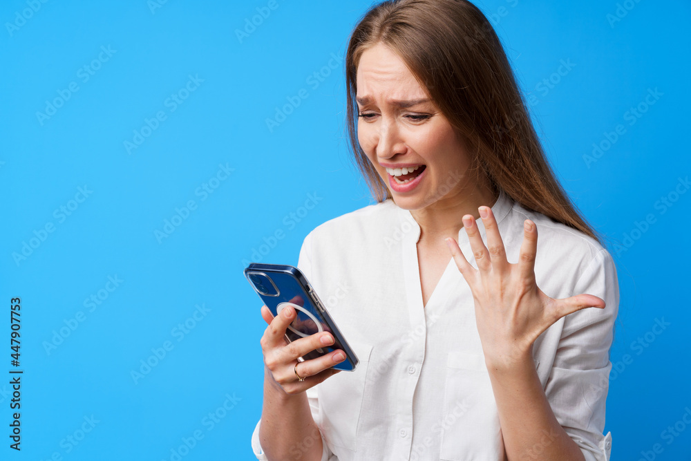 Portrait of young angry woman using her phone, annoyed texting with someone, blue background Portrait of young angry woman using her phone, annoyed texting with someone, blue background